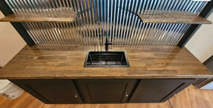 Stained wood counter with black sink under corrugated metal